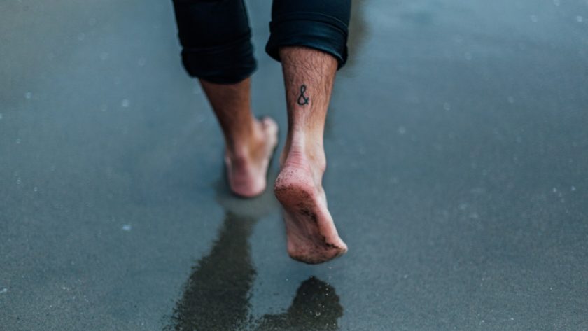 person with tattoo on foot walking on wet sands